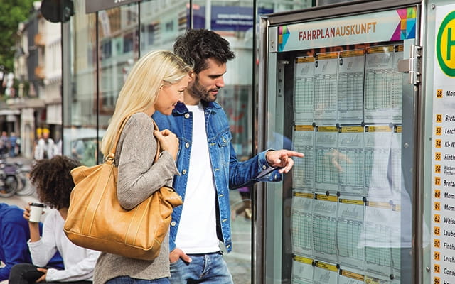 Junges Pärchen an einer Fahrplanauskunft der Mainzer Mobilität 2 Junges paar sucht auf den Fahrplänen nach der passenden Verbindung